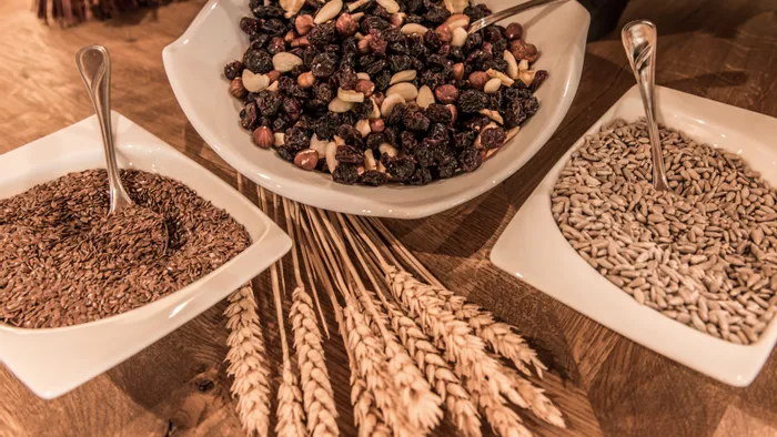 Assorted nuts, raisins, flaxseeds, and sunflower seeds in white bowls on wooden table